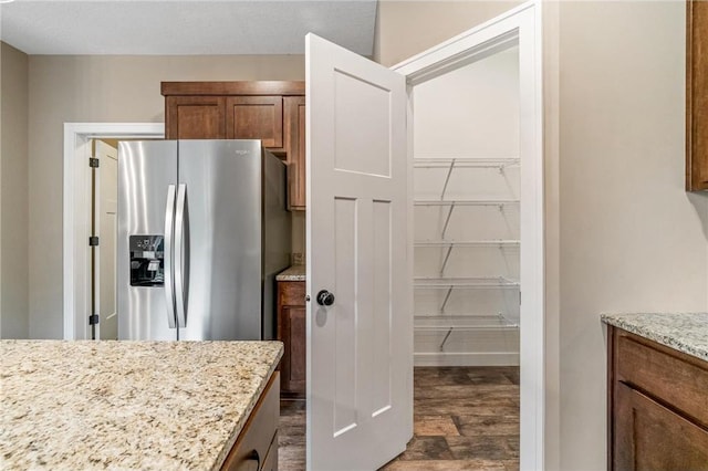 kitchen featuring stainless steel fridge with ice dispenser, brown cabinets, light stone counters, and dark wood finished floors
