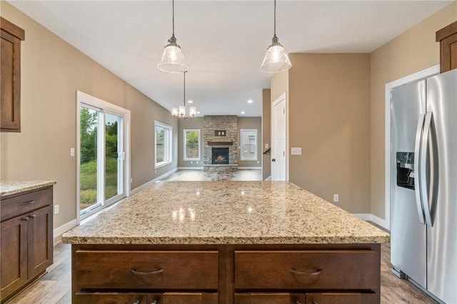 kitchen with a stone fireplace, stainless steel fridge, a kitchen island, light wood finished floors, and hanging light fixtures