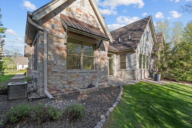 view of home's exterior featuring stone siding, central AC unit, a yard, and a standing seam roof