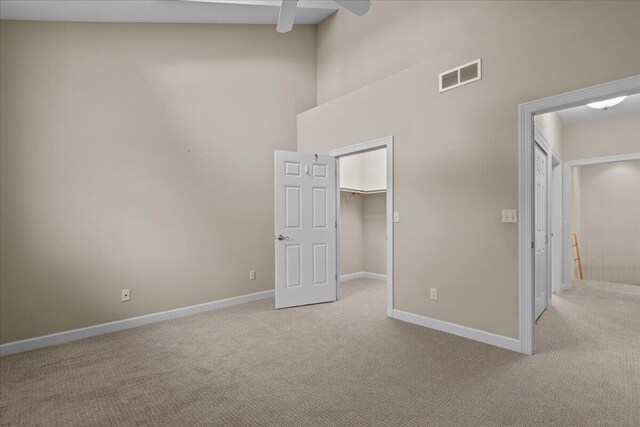 unfurnished bedroom with light carpet, a high ceiling, baseboards, a spacious closet, and a closet