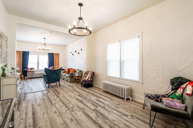 living area featuring wood finished floors, radiator heating unit, a textured wall, and an inviting chandelier
