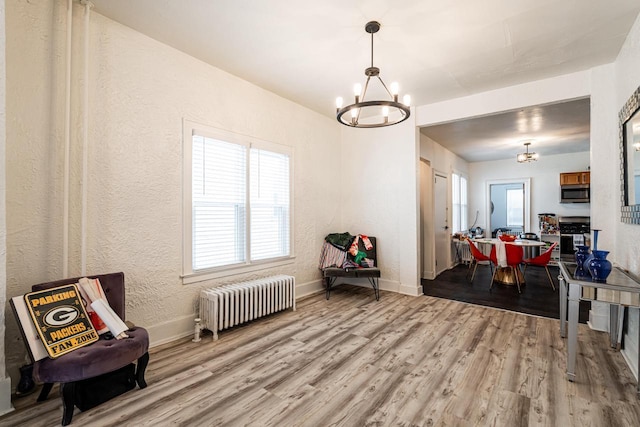sitting room with baseboards, wood finished floors, a notable chandelier, and radiator