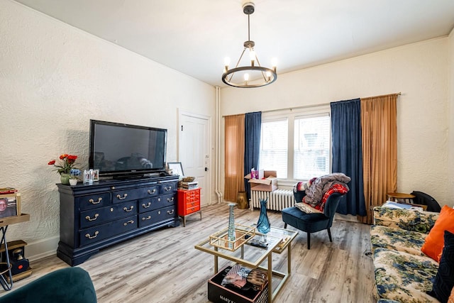 living room with a chandelier, baseboards, radiator heating unit, light wood-type flooring, and a textured wall