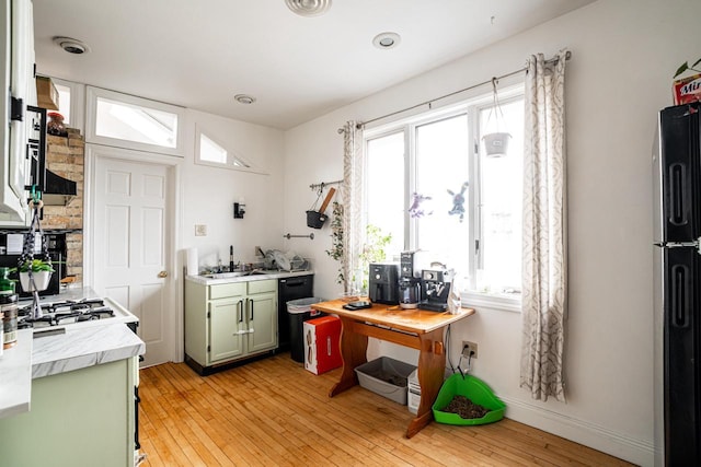 kitchen with green cabinetry, light countertops, freestanding refrigerator, light wood-type flooring, and baseboards