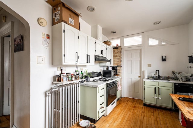 kitchen featuring green cabinets, radiator heating unit, white range with gas cooktop, under cabinet range hood, and a sink