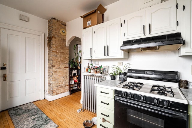 kitchen featuring range with gas cooktop, white cabinetry, radiator, under cabinet range hood, and arched walkways