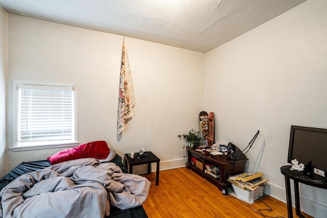 bedroom with baseboards, a textured ceiling, and light wood-type flooring