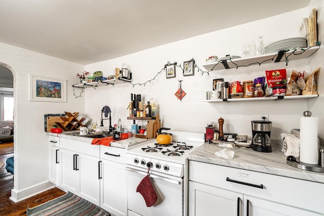 kitchen featuring light countertops, open shelves, a sink, arched walkways, and white range with gas cooktop