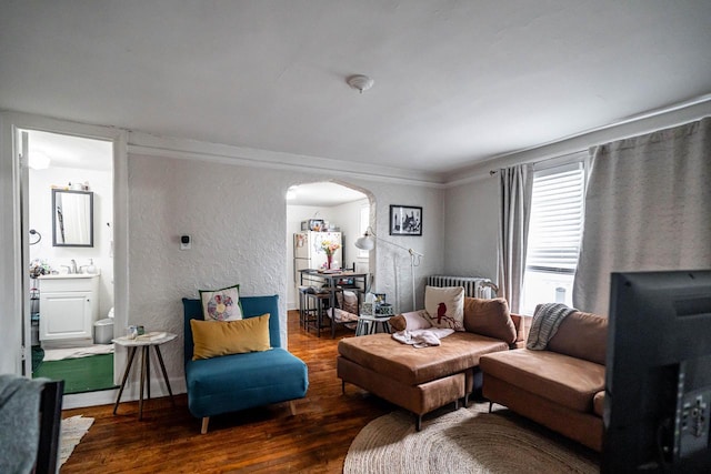 living area with wood finished floors, arched walkways, radiator heating unit, and a textured wall