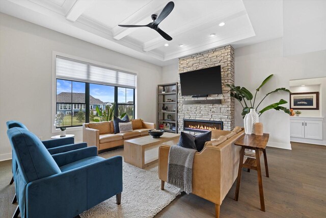 living area with crown molding, beamed ceiling, ceiling fan, a stone fireplace, and dark wood-style floors