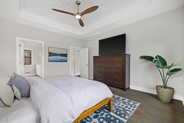 bedroom with dark wood-style flooring, a tray ceiling, baseboards, and visible vents
