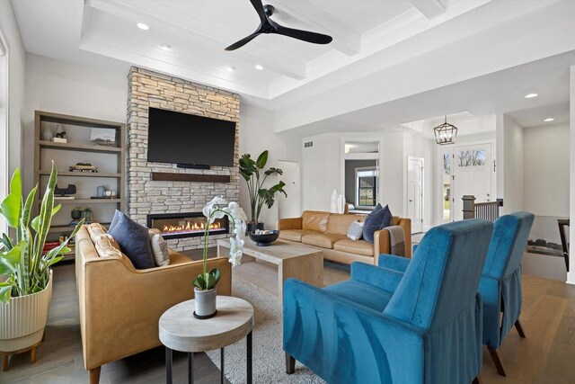 living area with beamed ceiling, ceiling fan, a stone fireplace, recessed lighting, and wood finished floors