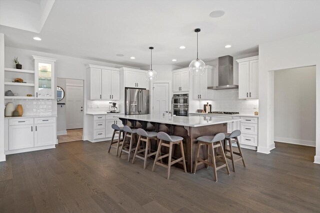 kitchen featuring wall chimney range hood, white cabinets, dark wood-type flooring, a kitchen bar, and appliances with stainless steel finishes
