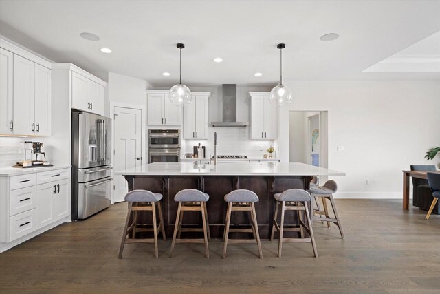 kitchen with light countertops, wall chimney exhaust hood, a kitchen bar, decorative backsplash, and appliances with stainless steel finishes