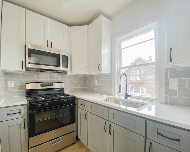 kitchen with stainless steel appliances, light countertops, a sink, and backsplash