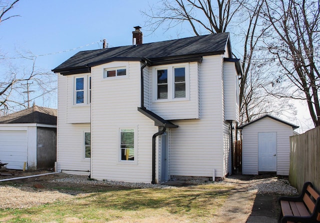 back of property featuring a storage shed, an outdoor structure, fence, a chimney, and a shingled roof