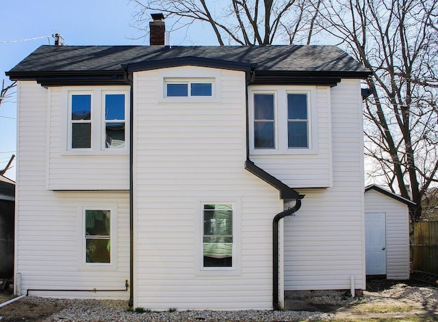 back of property with a shingled roof and a chimney