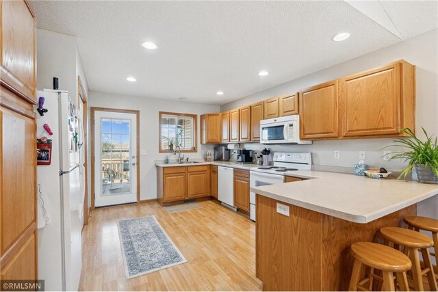 219 Bluff Dr, Somerset, WI 54025 - kitchen with white appliances, a kitchen bar, a peninsula, light countertops, and light wood finished floors