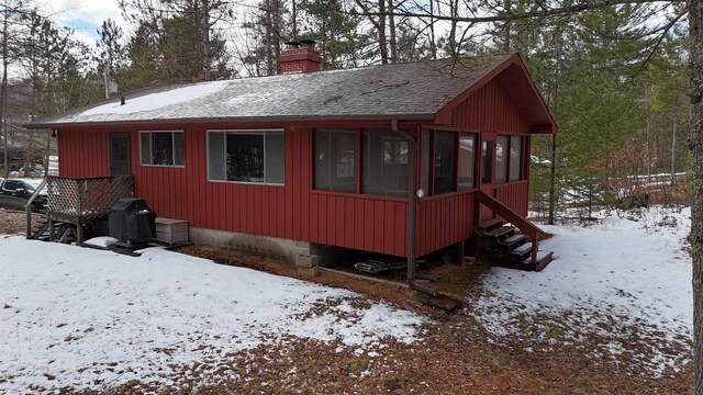 W1514 Spirit Ridge Trl, Keshena, WI 54135 - snow covered property featuring a shingled roof, a chimney, and a sunroom