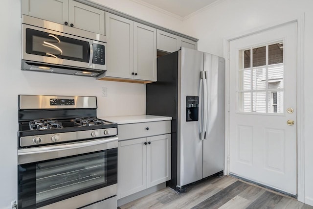 kitchen featuring light countertops, crown molding, stainless steel appliances, gray cabinets, and light wood-style flooring