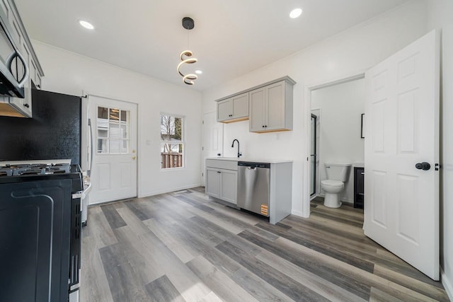 kitchen featuring gray cabinets, light countertops, stainless steel appliances, a sink, and wood finished floors