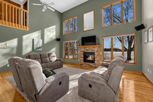 9842 Elan Rd, Tomah, WI 54660 - living area with a towering ceiling, wood-type flooring, a ceiling fan, a stone fireplace, and baseboards