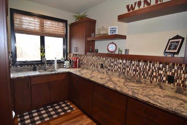 kitchen with open shelves, a sink, light wood-style floors, backsplash, and stone countertops