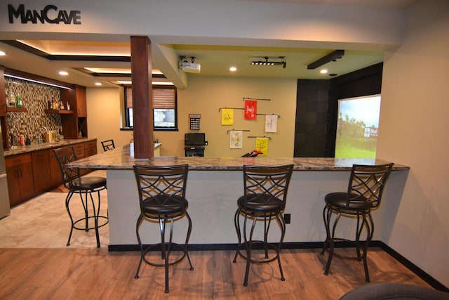 bar featuring indoor wet bar, tasteful backsplash, baseboards, and light wood-style flooring