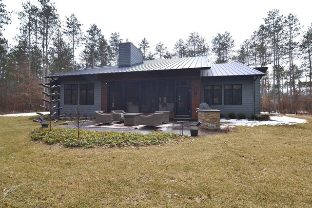 back of property with an outdoor living space, a lawn, a patio area, metal roof, and a chimney