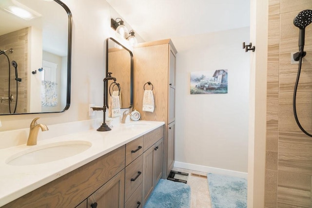 bathroom featuring tiled shower, double vanity, baseboards, and a sink