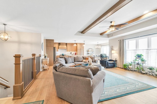 living area with light wood-type flooring, ceiling fan with notable chandelier, and beamed ceiling
