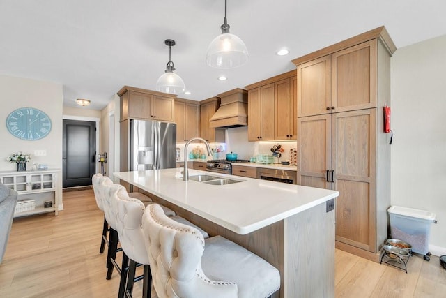 kitchen with custom range hood, light wood-style flooring, stainless steel refrigerator with ice dispenser, a breakfast bar area, and a sink