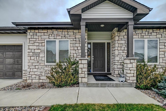 view of exterior entry with a garage, stone siding, and covered porch
