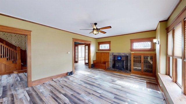 unfurnished living room featuring a wood stove, a ceiling fan, wood finished floors, stairs, and baseboards