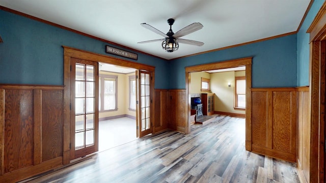 unfurnished room with a ceiling fan, ornamental molding, a wainscoted wall, and wood finished floors