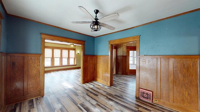 unfurnished room featuring a wainscoted wall, visible vents, ceiling fan, a healthy amount of sunlight, and wood finished floors