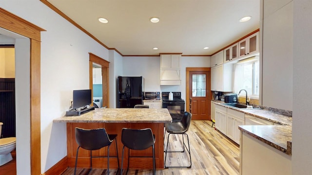 kitchen with white cabinets, a sink, a peninsula, black appliances, and light wood finished floors