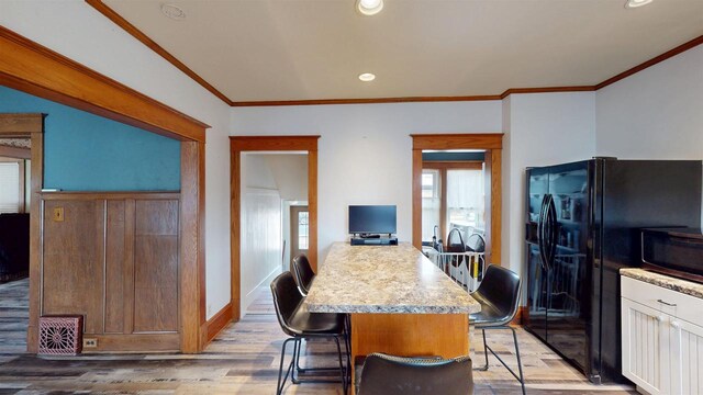 kitchen with baseboards, a breakfast bar, ornamental molding, light countertops, and light wood finished floors