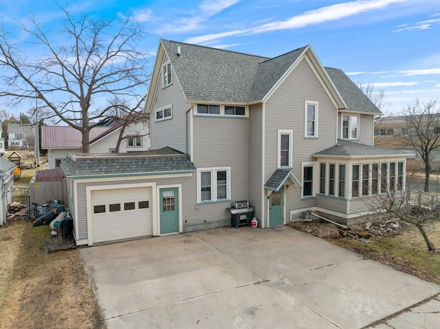 back of house featuring an attached garage, a shingled roof, driveway, and a sunroom