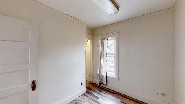 empty room with light wood-style flooring, baseboards, and crown molding