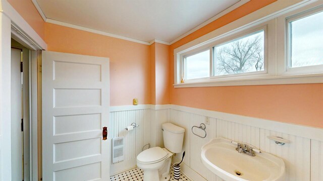 bathroom featuring a sink, toilet, heating unit, crown molding, and a wainscoted wall