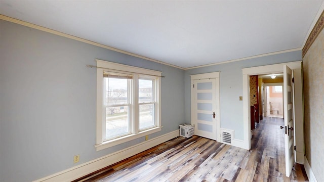 spare room with visible vents, baseboards, ornamental molding, and wood finished floors