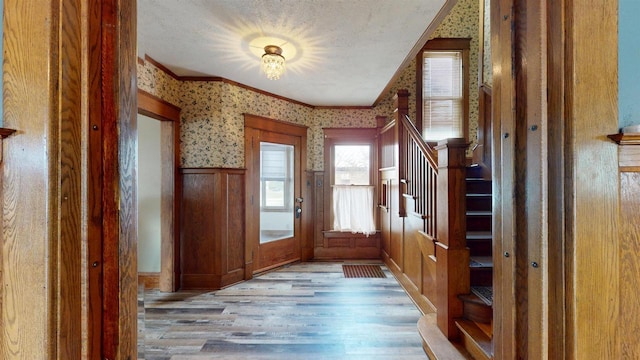foyer with light wood-style floors, crown molding, a wainscoted wall, stairs, and wallpapered walls