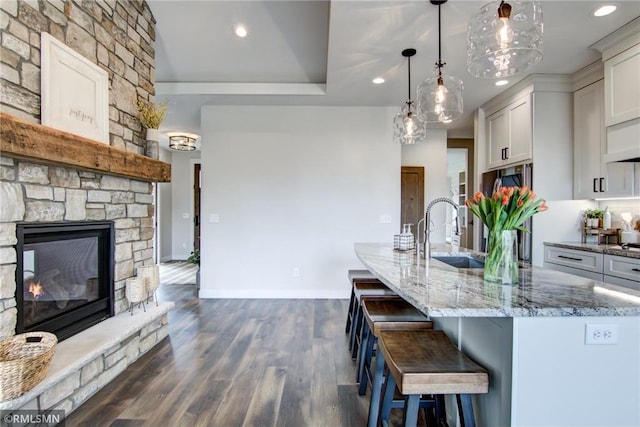 kitchen with a sink, a stone fireplace, recessed lighting, and light stone countertops