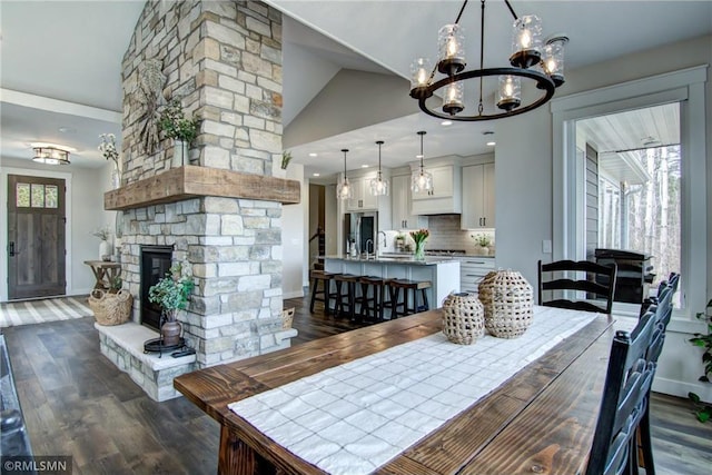dining room featuring high vaulted ceiling, an inviting chandelier, dark wood finished floors, a stone fireplace, and baseboards
