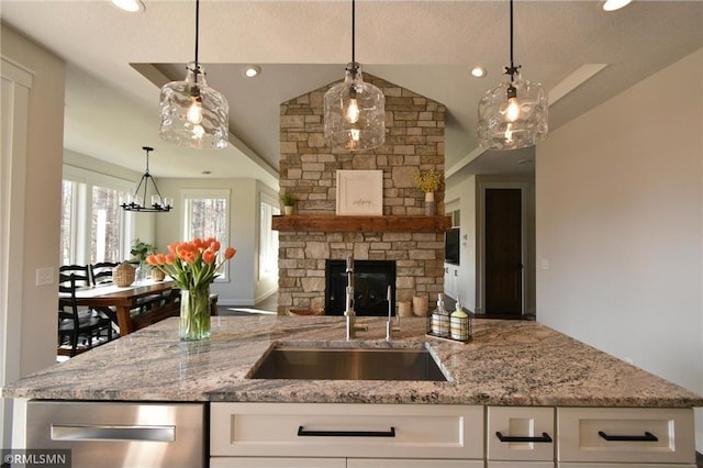 kitchen with a sink, a stone fireplace, white cabinets, and light stone countertops