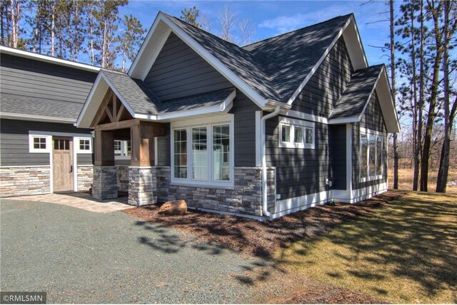view of side of property with roof with shingles, stone siding, and a lawn