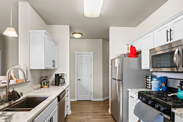 kitchen with dark wood finished floors, white cabinets, appliances with stainless steel finishes, light stone counters, and a sink
