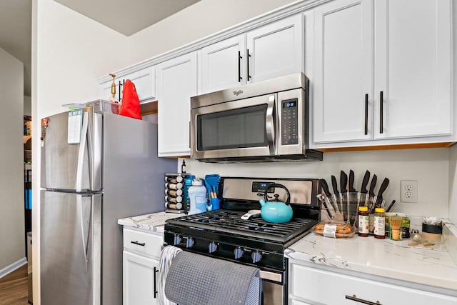kitchen with wood finished floors, light stone counters, white cabinets, and stainless steel appliances