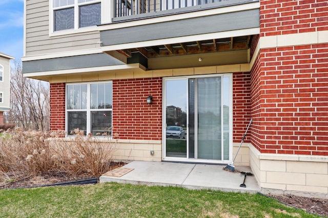 view of exterior entry with a balcony, a patio area, and brick siding